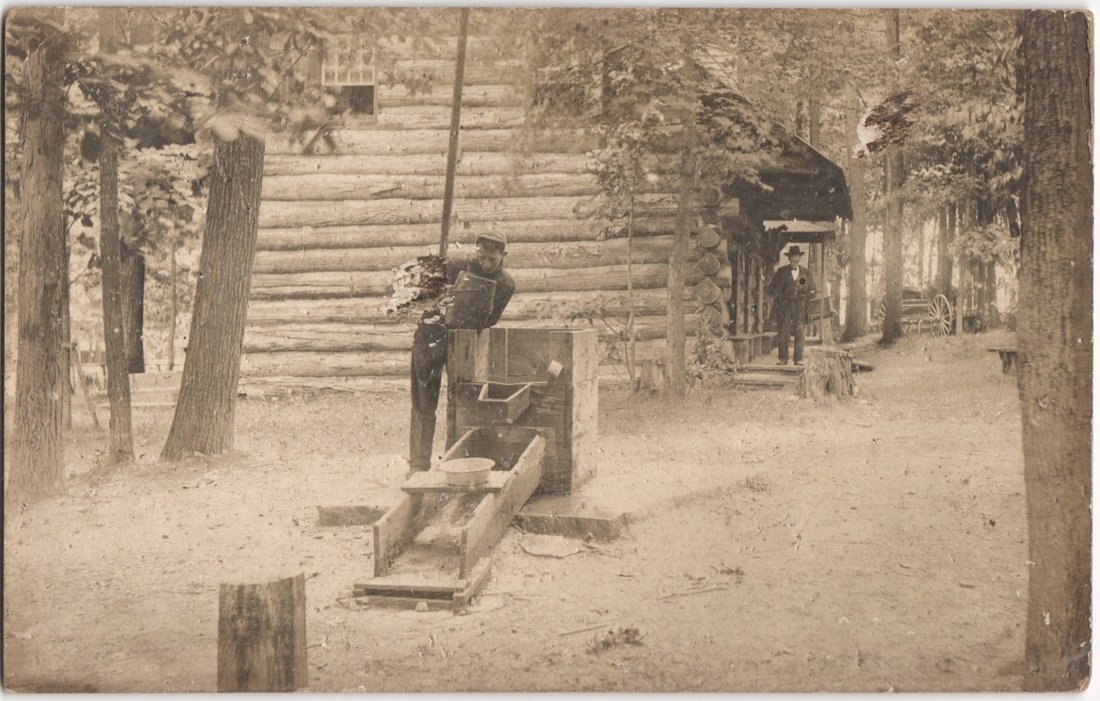 Two men with a sluice box at a rustic log cabin, early 20th century postcard
